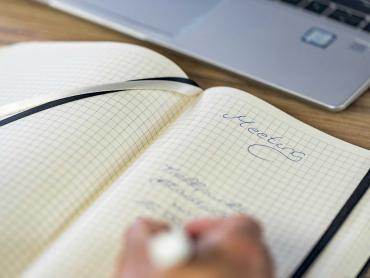 Person erstellt Notizen in Notizbuch zu einem Meeting