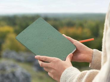 Frau hält Re-Up Notizbuch in der Natur in den Händen