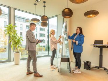 Drei Kollegen arbeiten in Büro gemeinsam an Whiteboard