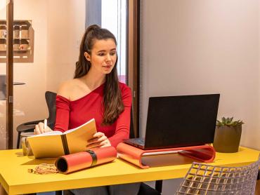 Frau schaut in Laptop und hält Notizbuch in den Händen