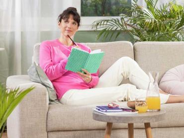 Frau sitzt auf Sofa, hält Notizbuch in Händen und schaut nachdenklich
