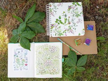 Jolie „Fairytale Garden“ Spiral-Notizbuch liegt auf Rasen mit Wassermalfarben