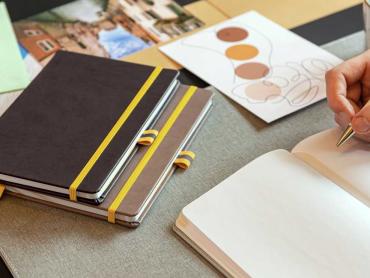 Notizbücher liegen auf Schreibtisch. Hand schreibt in ein Notizbuch.