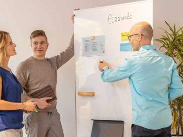 Drei Personen stehen um mobiles Whiteboard herum und arbeiten damit