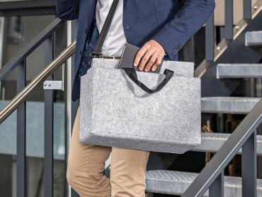 Ein Businessman hat eine Desk Sharing Tasche umhängen und greift in die Tasche und holt ein Notizbuch heraus