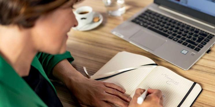 Frau arbeitet an Laptop und schreibt in Notizbuch