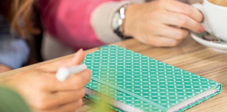 Frau hält Kugelschreiber in der Hand um in Notizbuch zu schreiben