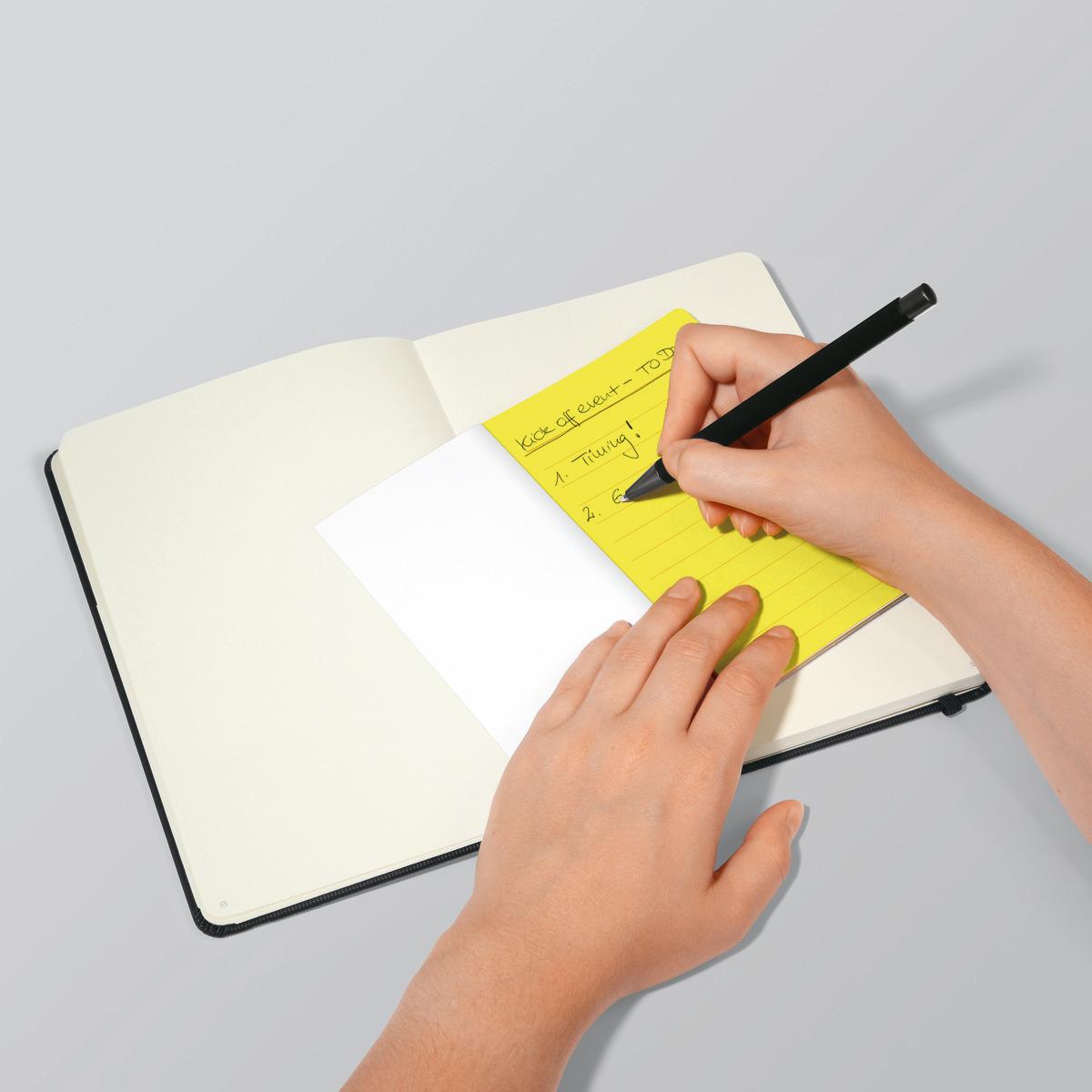 Hands writing notes on yellow paper in an open notebook