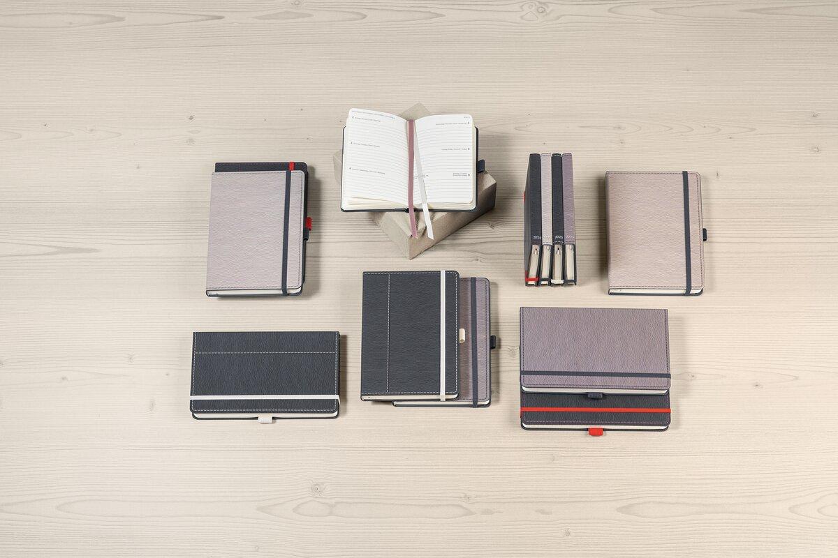 Notizbücher in verschiedenen Größen und Farben auf einem Holztisch Ein geöffnetes Buch in der Mitte