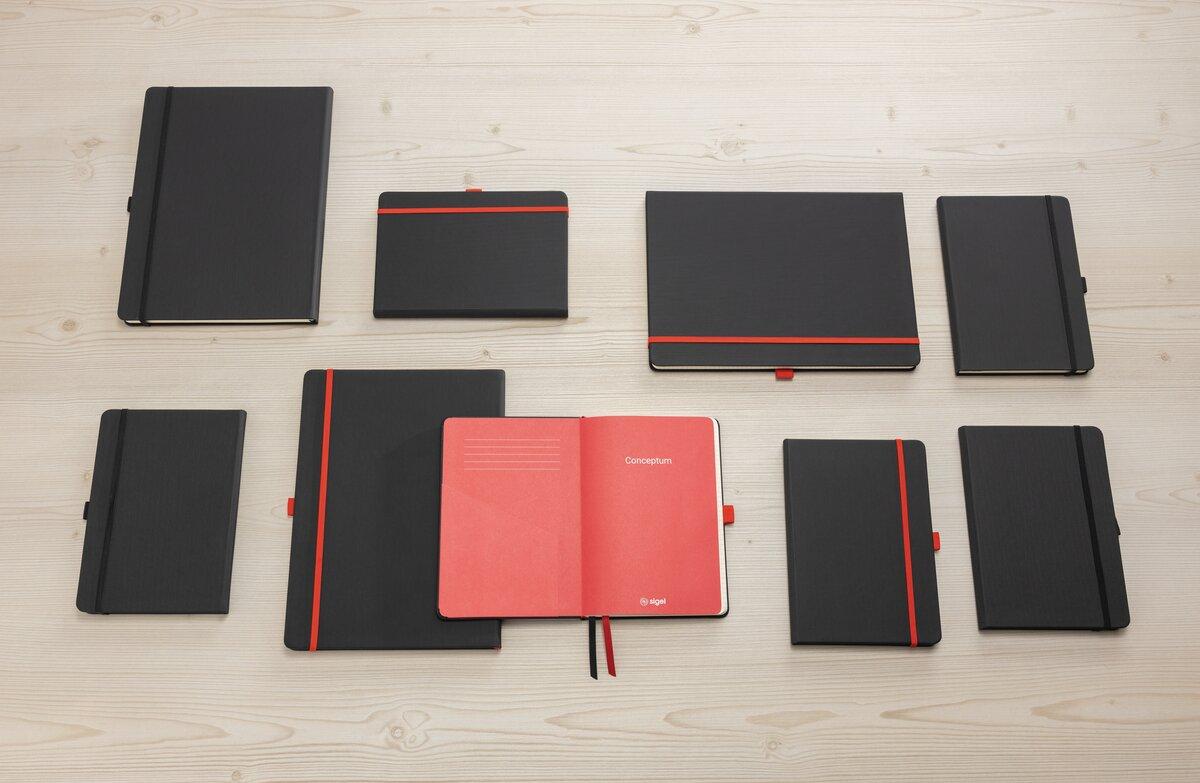 Schwarze Notizbücher mit roten Akzenten liegen auf hellem Holztisch Ein geöffnetes Notizbuch zeigt rote Innenseiten