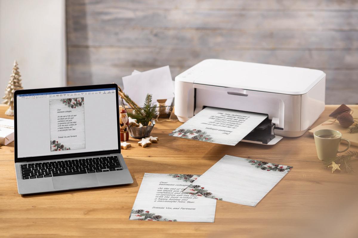Laptop and printer on wooden desk, Christmas card is printed