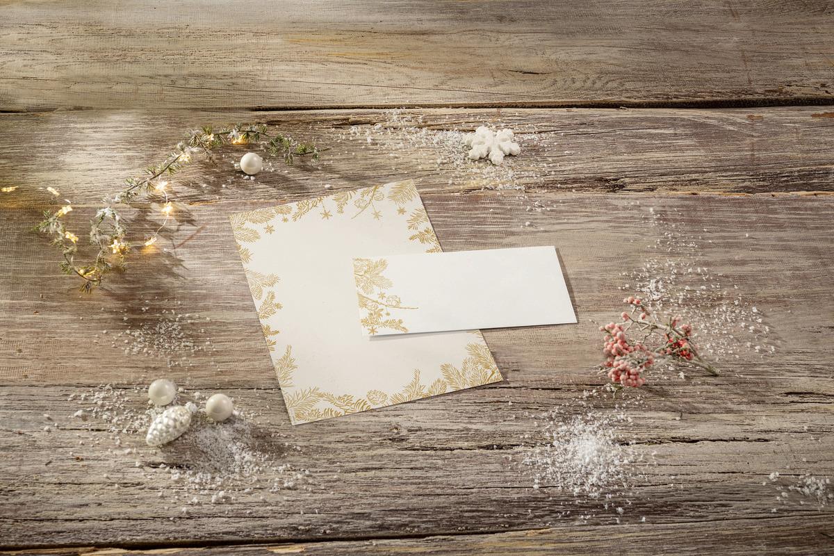 Envelopes with golden patterns on wooden table surrounded by winter decoration