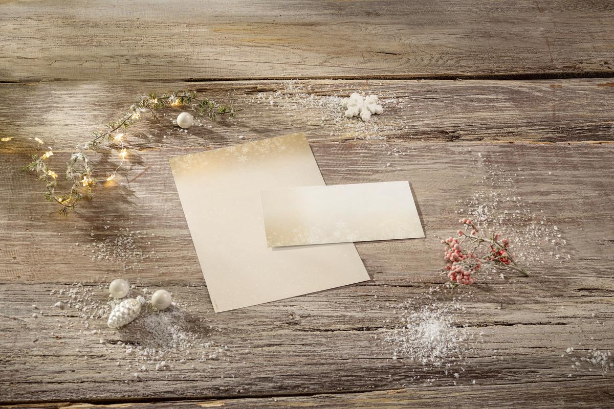 Card with envelope on wooden table surrounded by fairy lights and snow decoration