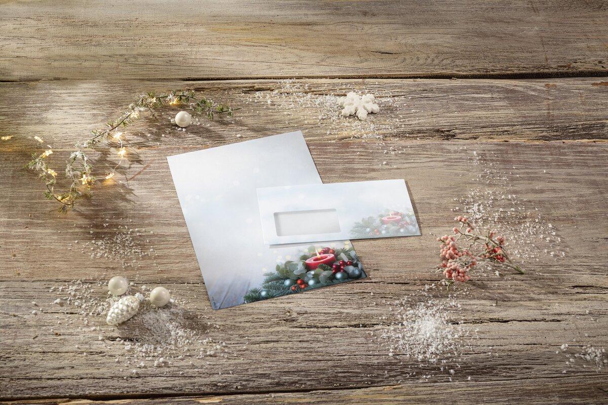 Postcard and envelope with Christmas décor on wooden table, string lights and artificial snow