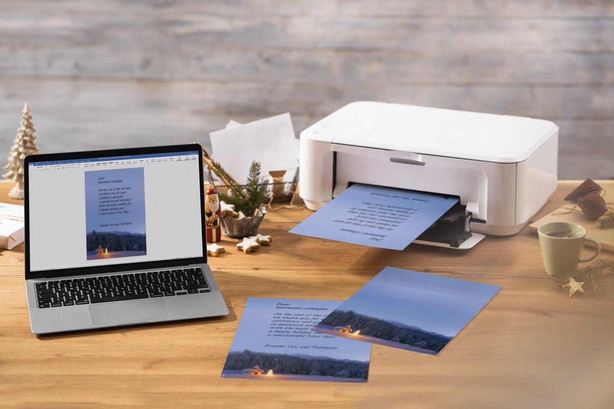 Laptop and printer on wooden table, printing Christmas cards