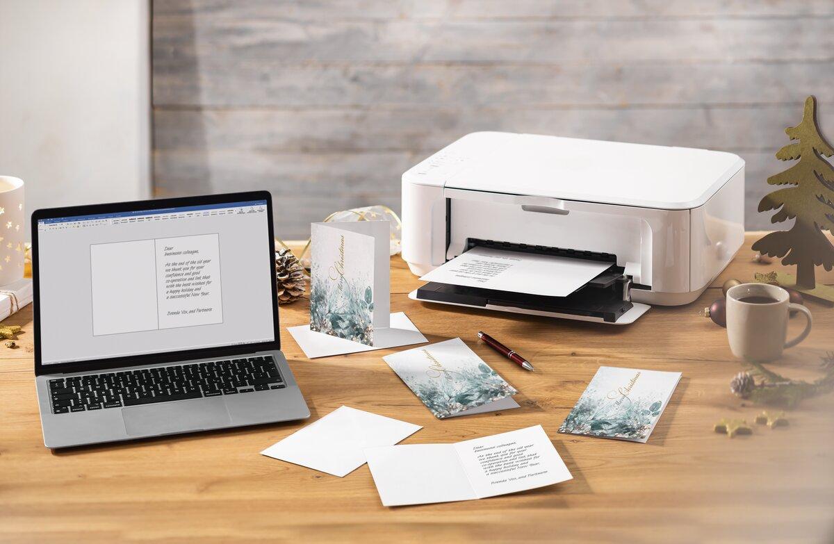 Laptop and printer on wooden table with Christmas cards