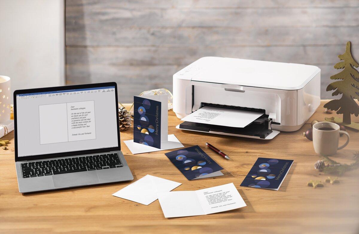 Laptop and printer on wooden table with Christmas cards