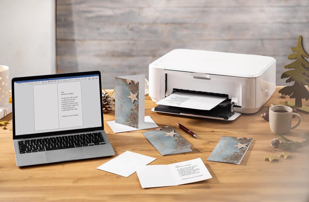 Laptop and printer on wooden desk surrounded by Christmas cards and a cup