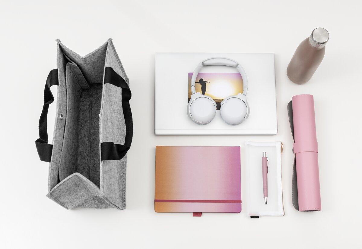 Graue Tasche, Laptop, Kopfhörer, Wasserflasche, Notizbuch, Stiftemäppchen auf weißer Fläche