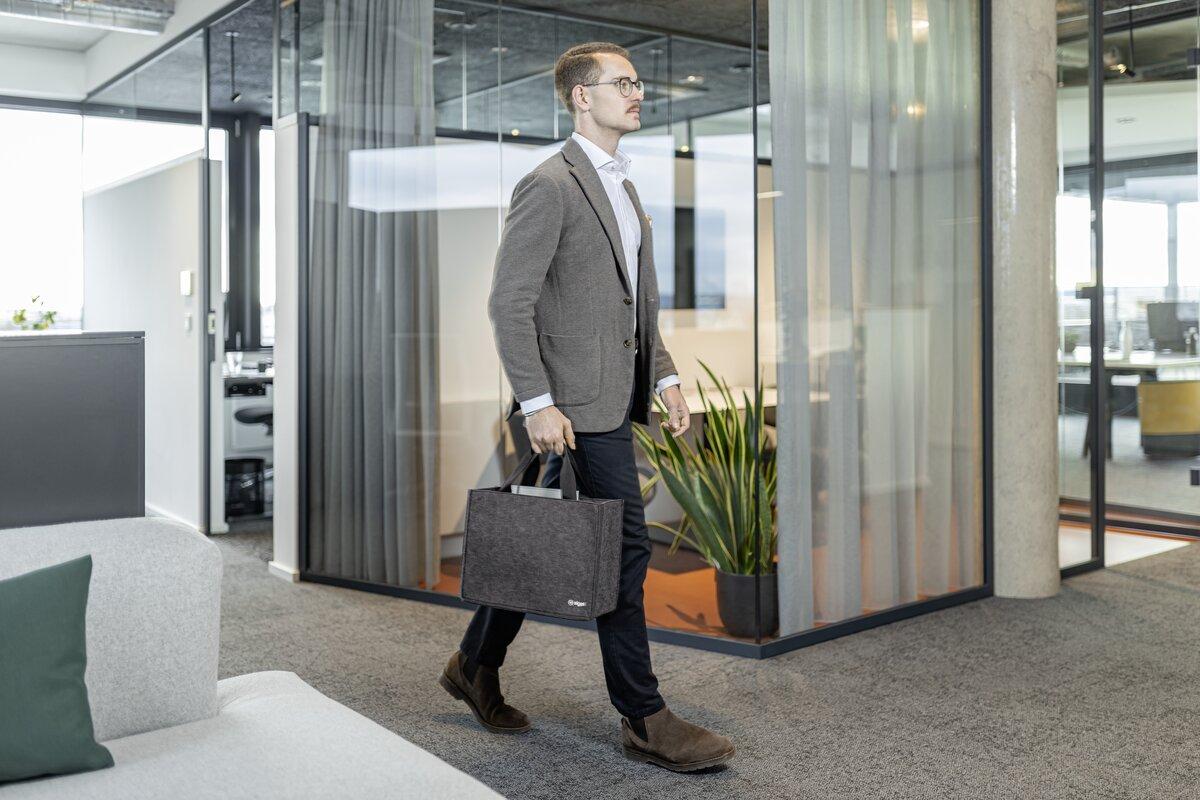 Person in Büro, trägt Anzug und Tasche