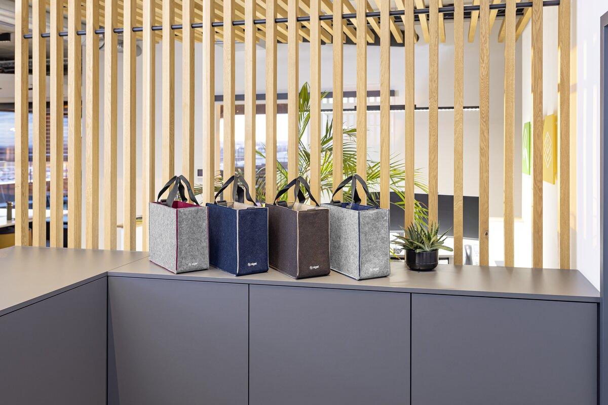 Vier Filztaschen auf einem Tisch vor Holzlamellen und Pflanzen