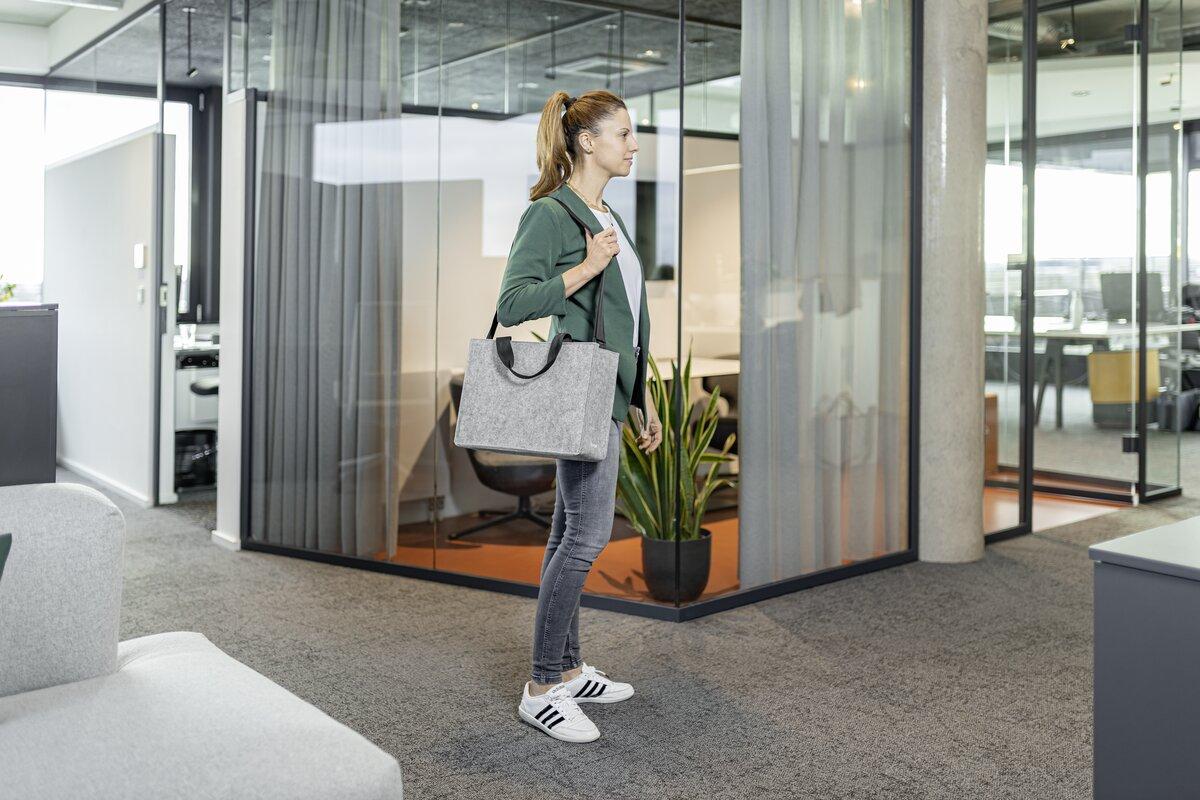 Person mit grüner Jacke und Tasche im modernen Büroflur