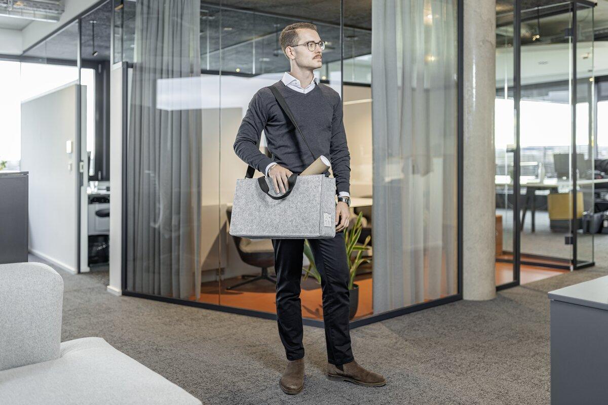 Mann in Büro hält graue Tasche