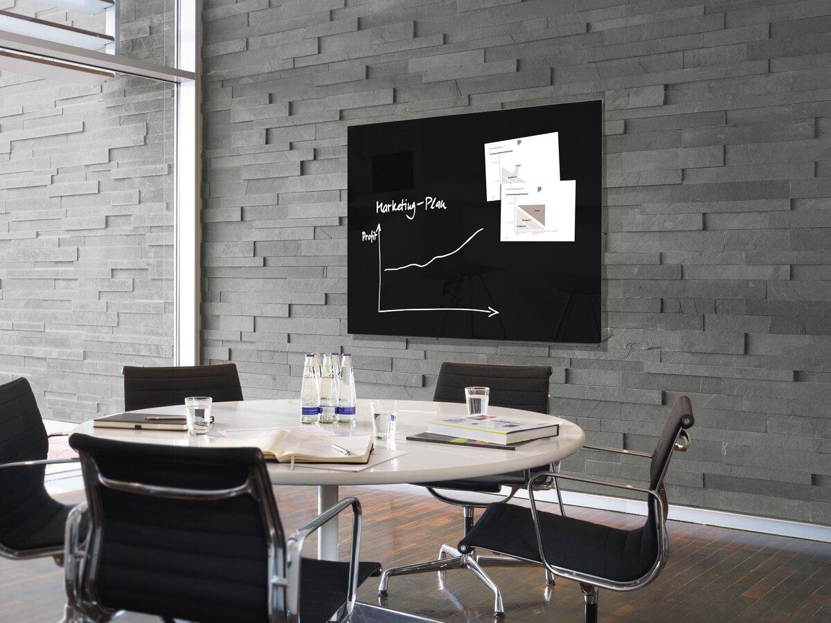 Konferenzraum mit Tisch, Stühlen und Wandtafel mit Grafiken