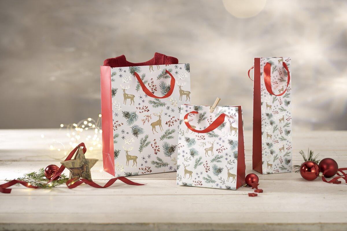 Gift bags with reindeer, fir branches and red ornaments on white table