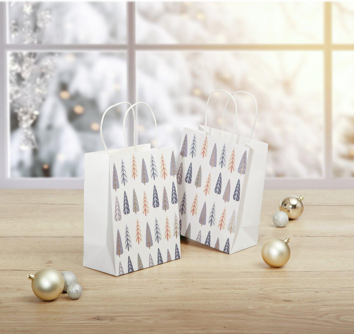 White Gift Bags with Tree Pattern, Golden and Silver Balls on Wooden Surface, Blurred Snow Background