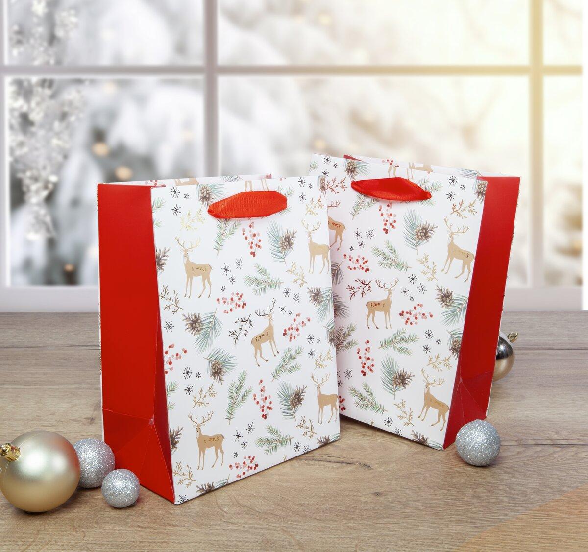 Two deer and pine needle pattern gift bags on a table in front of a snowy window