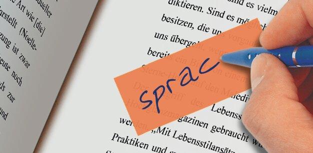 Hand holding blue pen, writing on orange piece of paper over printed text