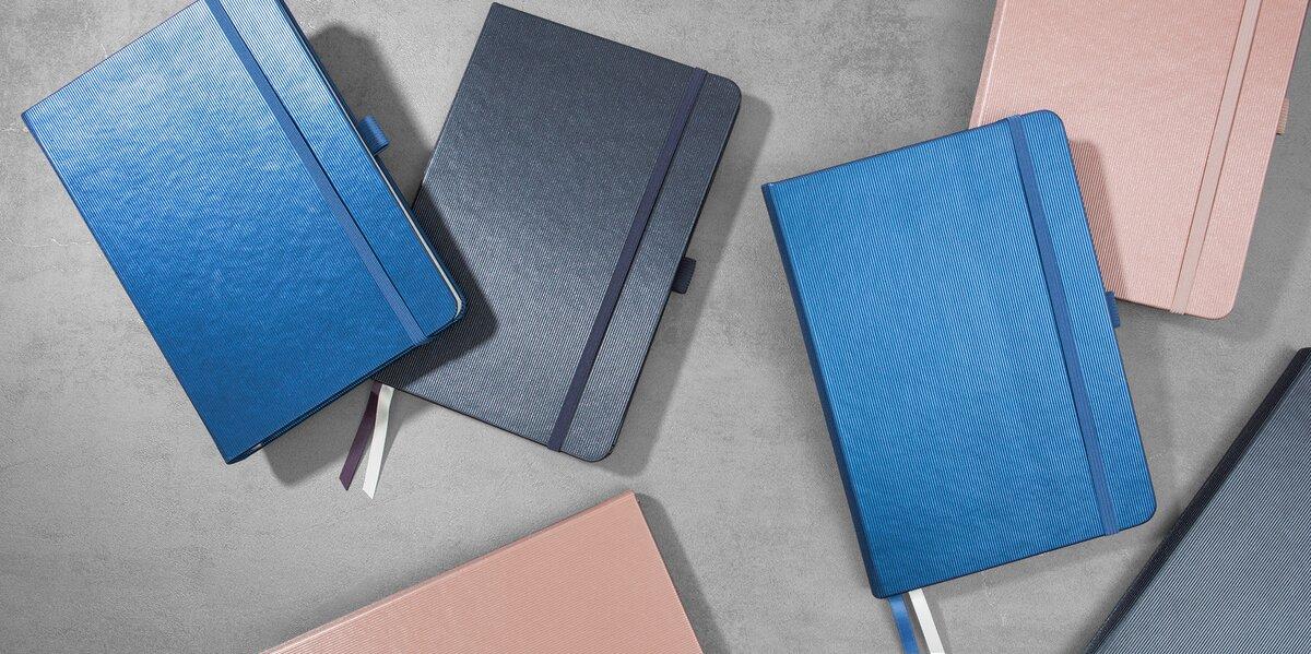 Mehrere Notizbücher in Blau und Rosa auf grauem Hintergrund