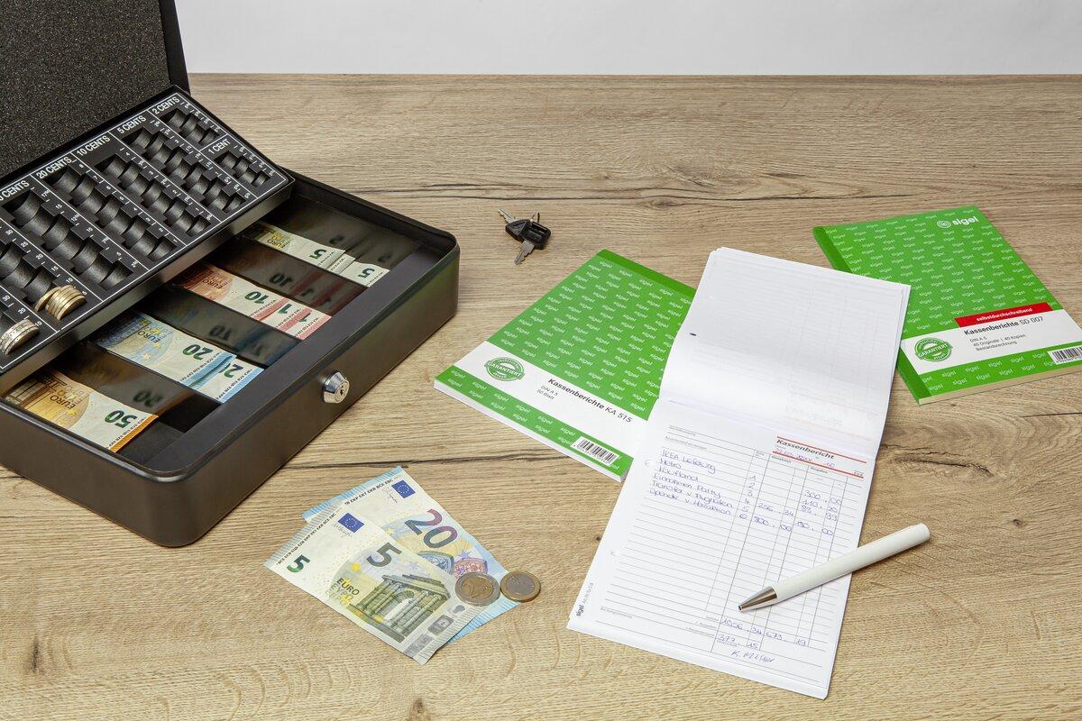 Kassenlade mit Euro-Banknoten und -münzen, daneben Notizblock und Stift