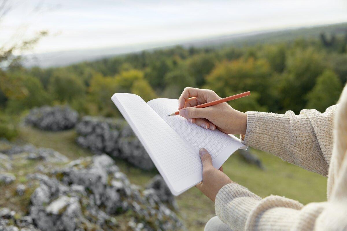 Hände halten Notizbuch und Stift, Hintergrund ist bewaldet