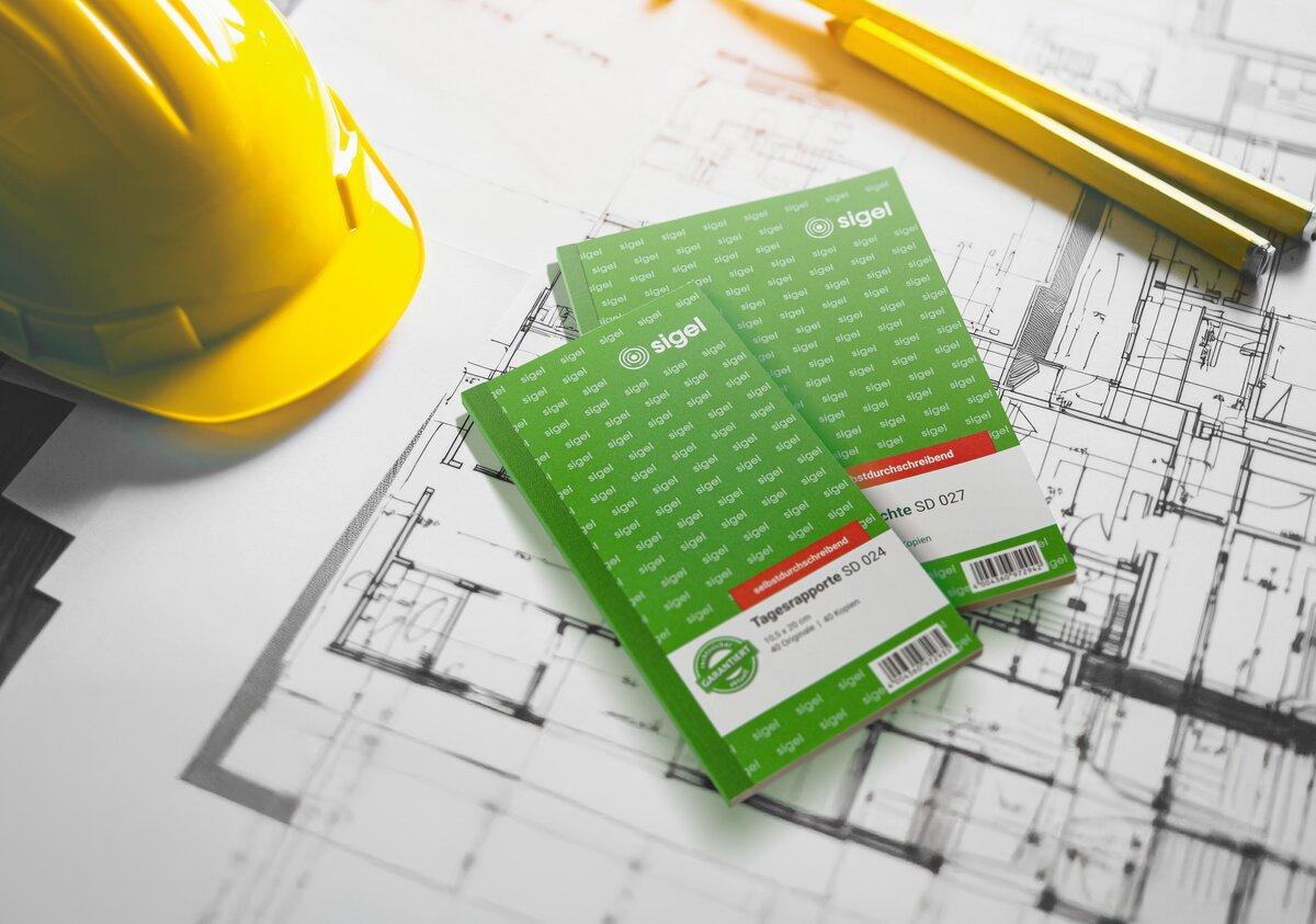 Gelber Bauhelm und grüne Blöcke mit Bauplänen