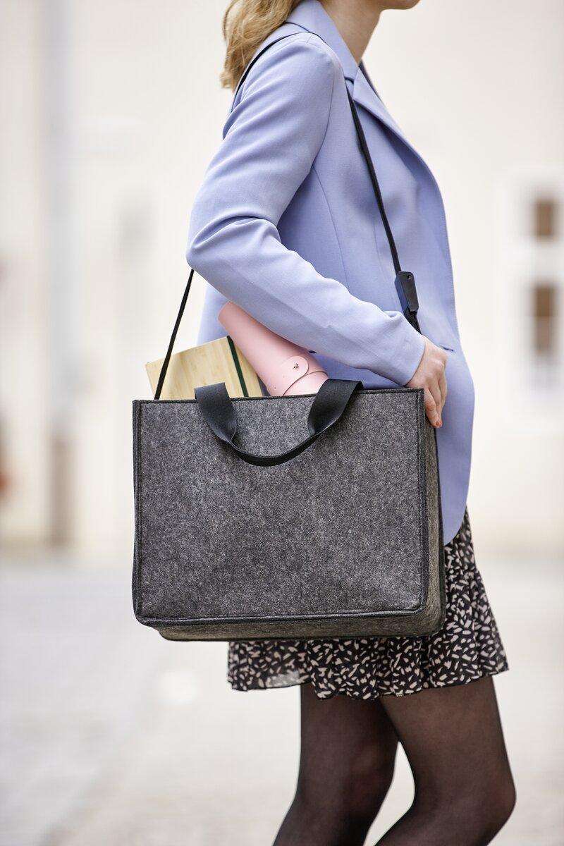 Person mit hellblauem Mantel trägt graue Tasche, Inhalt sichtbar