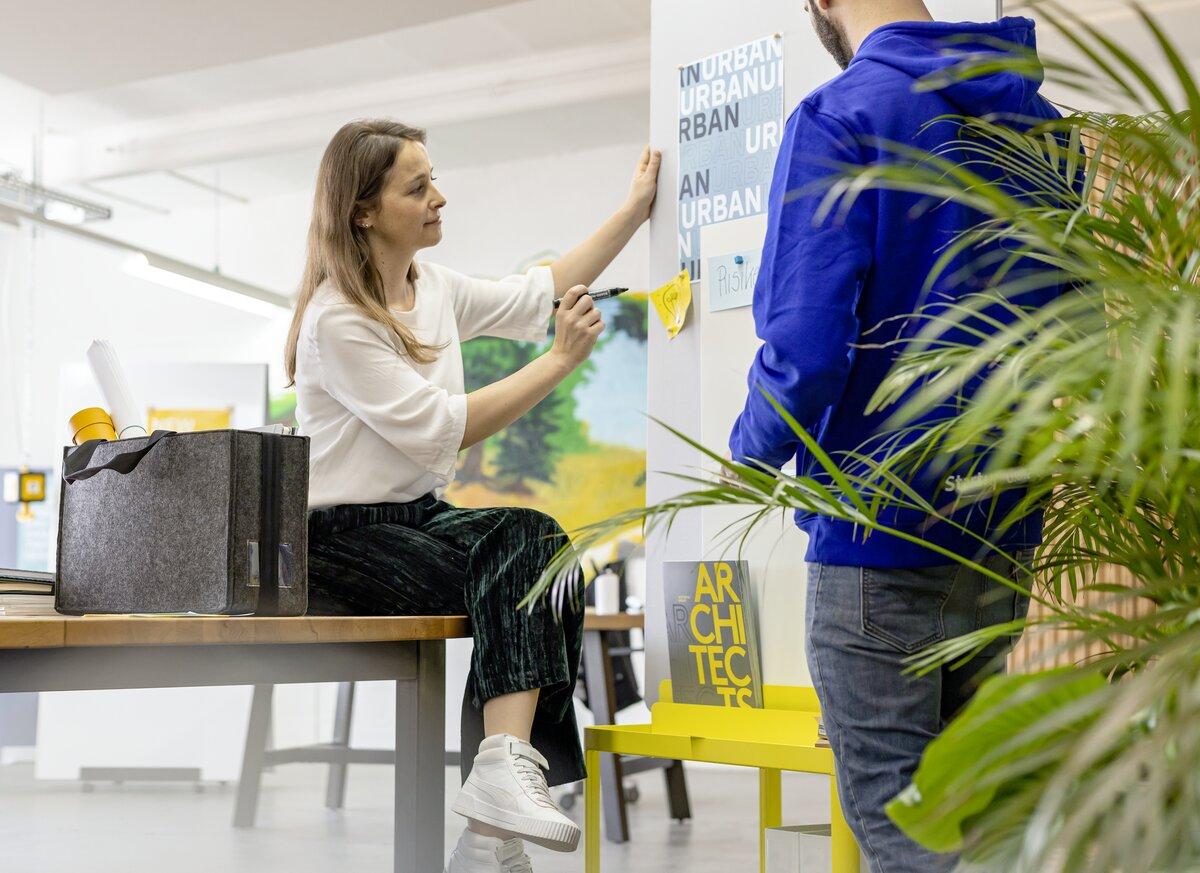 Person pinnt Notiz an Wand, daneben eine Person in blauem Hoodie