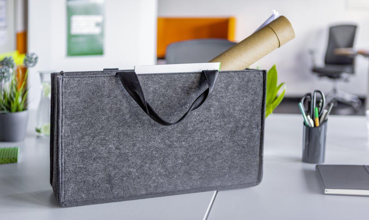 Graue Filztragetasche mit Rollen und Papieren auf einem Schreibtisch