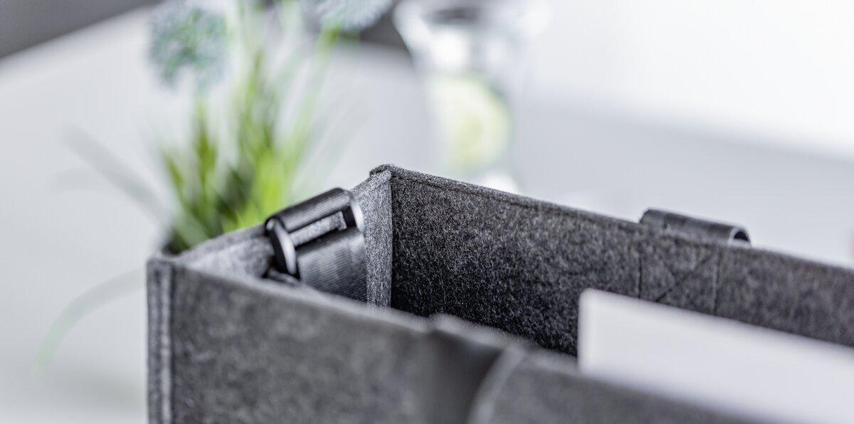 Graue Filzbox mit Schnallen, unscharfe Pflanze im Hintergrund