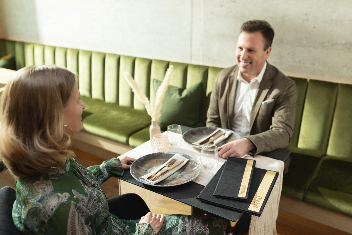 Two people at table in restaurant green upholstered bench in the background