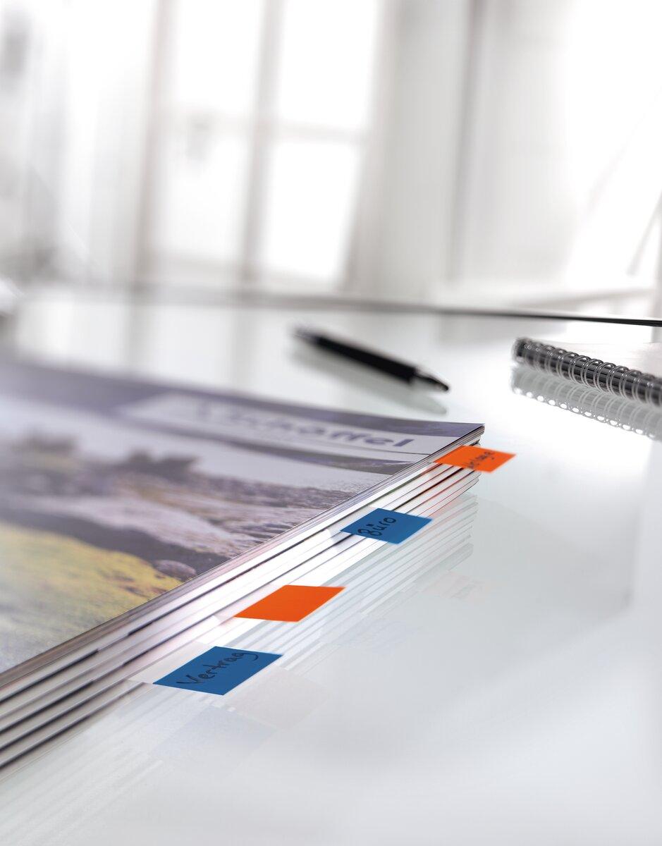 Document with colored tabs on a glass table, next to it a pen and a notepad