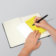 Hands writing notes on yellow paper in an open notebook