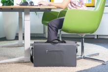 Graue Aktentasche unter grünem Bürostuhl neben Tisch