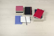 Mehrere bunte Kalender auf hellem Holztisch Ein geöffneter Kalender zeigt seine Seiten