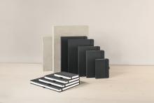 Schwarze Notizbücher in verschiedenen Größen auf Holzfläche vor hellgrauen Blöcken
