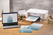 Laptop and printer printing Christmas cards on wooden desk