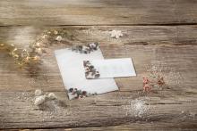 Christmas envelope and card with pine cone motif on wooden table, fairy lights and decorative elements