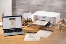 Laptop and printer on wooden table, printed Christmas cards
