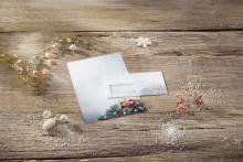 Postcard and envelope with Christmas décor on wooden table, string lights and artificial snow